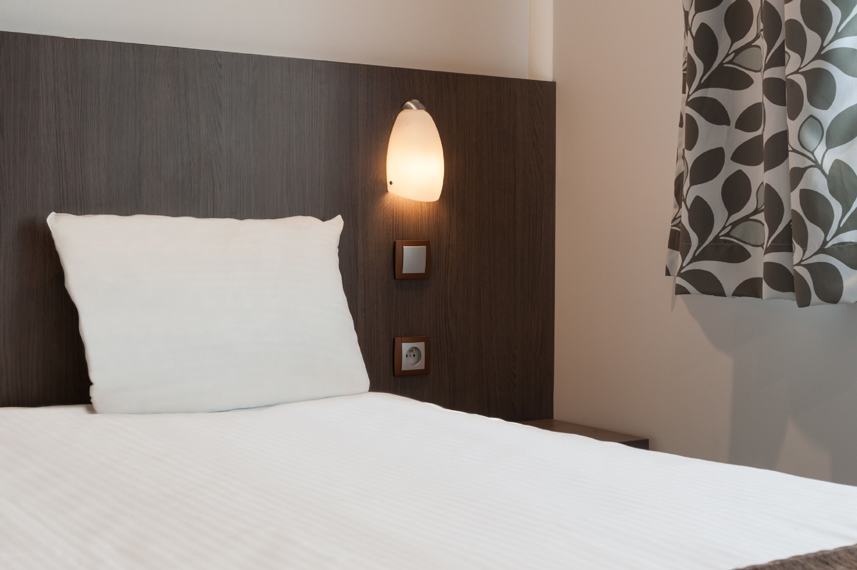 A neatly made bed with a white pillow and a headboard with a wall-mounted light fixture.