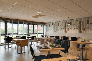 Un comedor moderno con mesas y sillas, ventanas amplias y un muro con diseño.