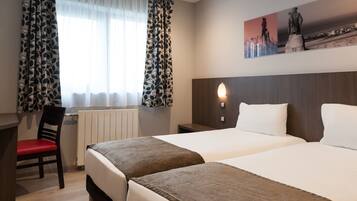 Habitación de hotel con dos camas, un escritorio, una silla y un ventanal con cortinas estampadas.