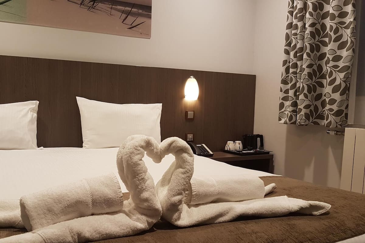 Une chambre d’hôtel avec un lit soigneusement fait, une table de chevet avec une machine à café et une lampe fixée au mur.