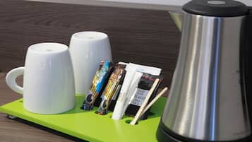 A coffee station with two white mugs, a stainless steel coffee pot, and several coffee packets on a green tray.