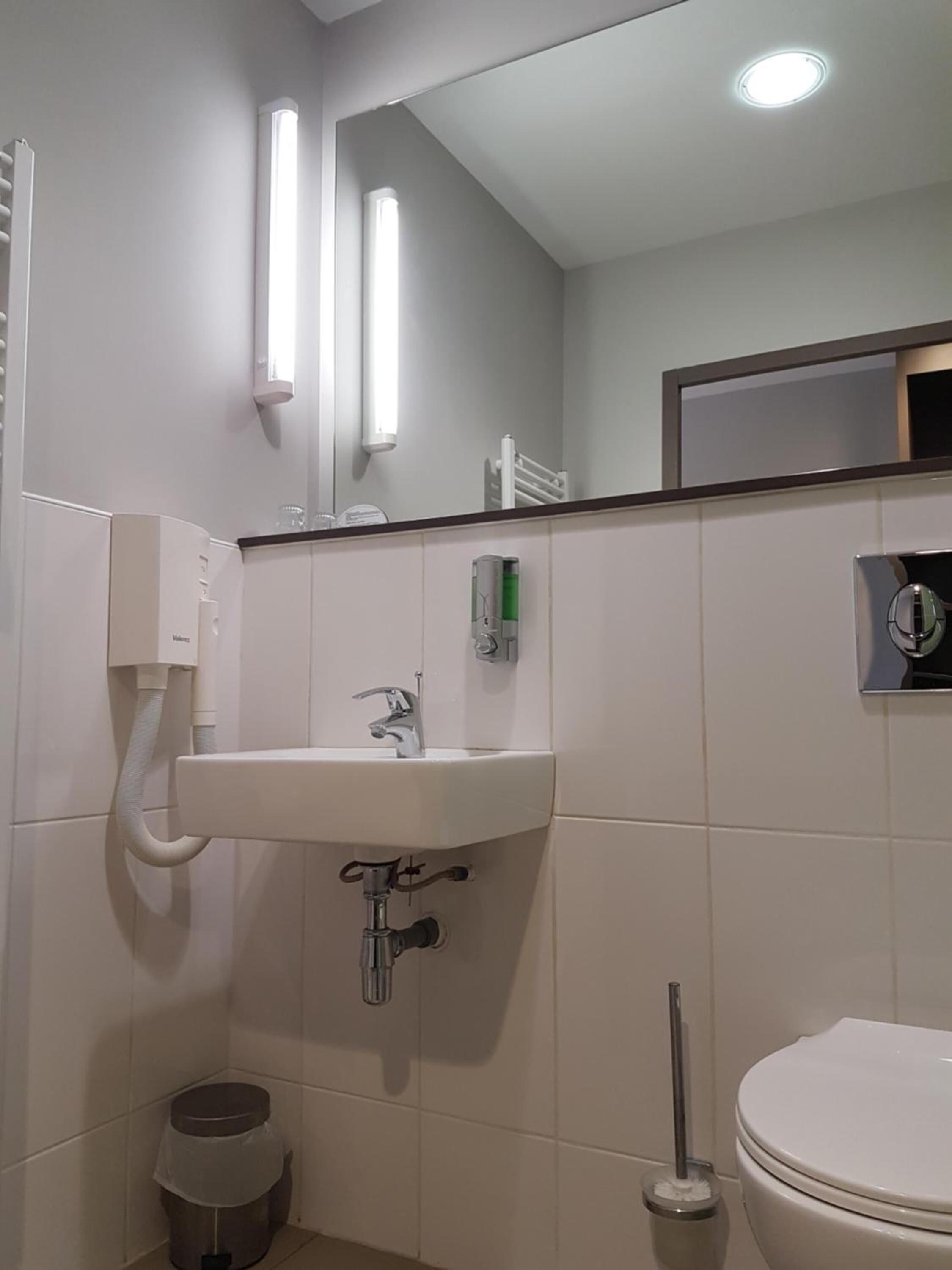 Un baño con lavamanos, espejo e inodoro blancos.