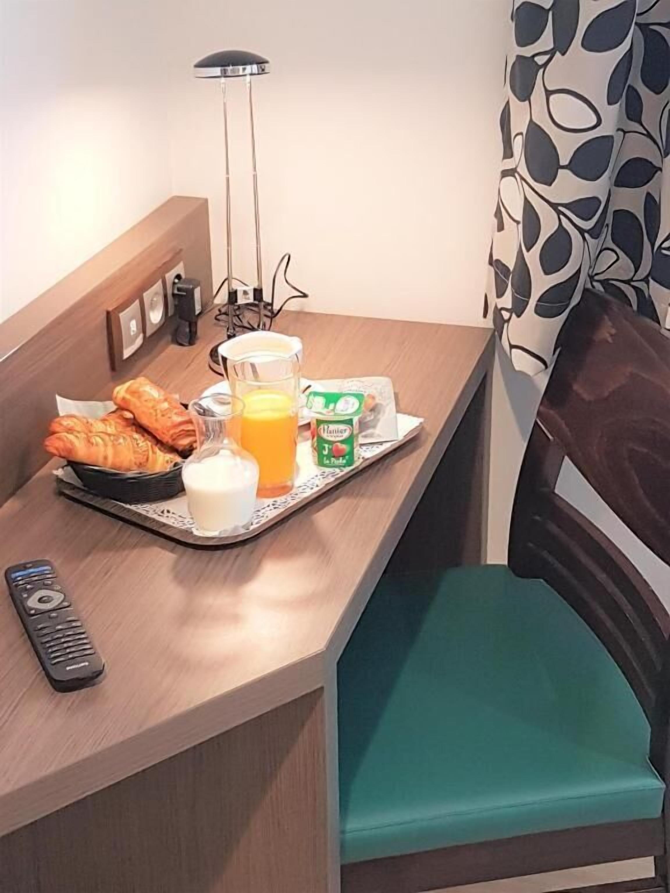 Un vassoio colazione con croissant, succo d'arancia e un pacchetto di latte su un tavolo di legno.