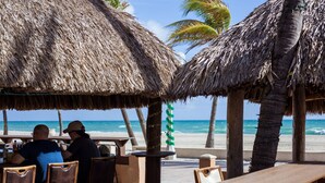 Un restaurante frente al mar con sombrillas de paja, mesas y sillas de madera.