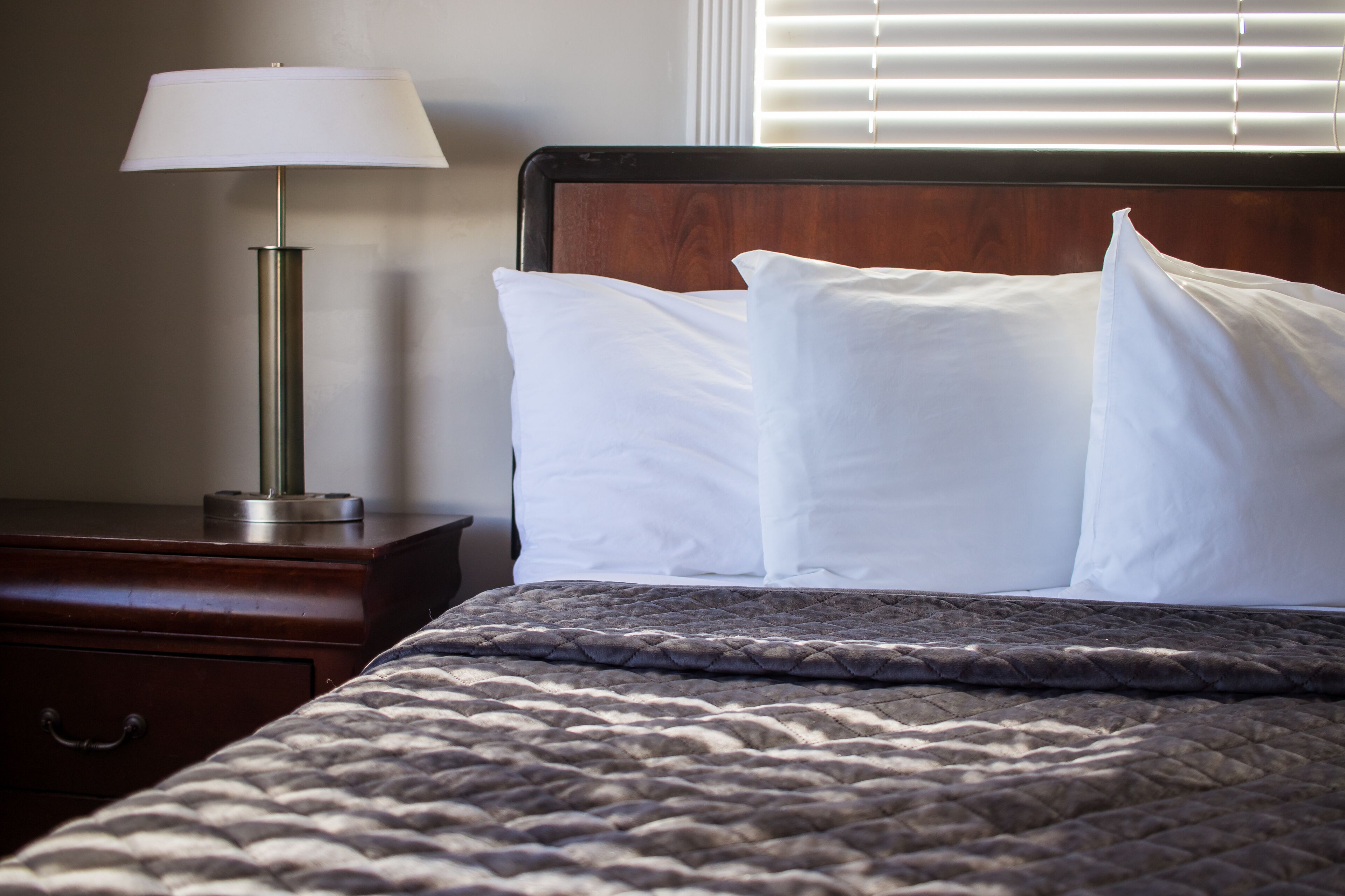 A neatly made bed with a dark quilt, a bedside lamp, and a wooden nightstand.