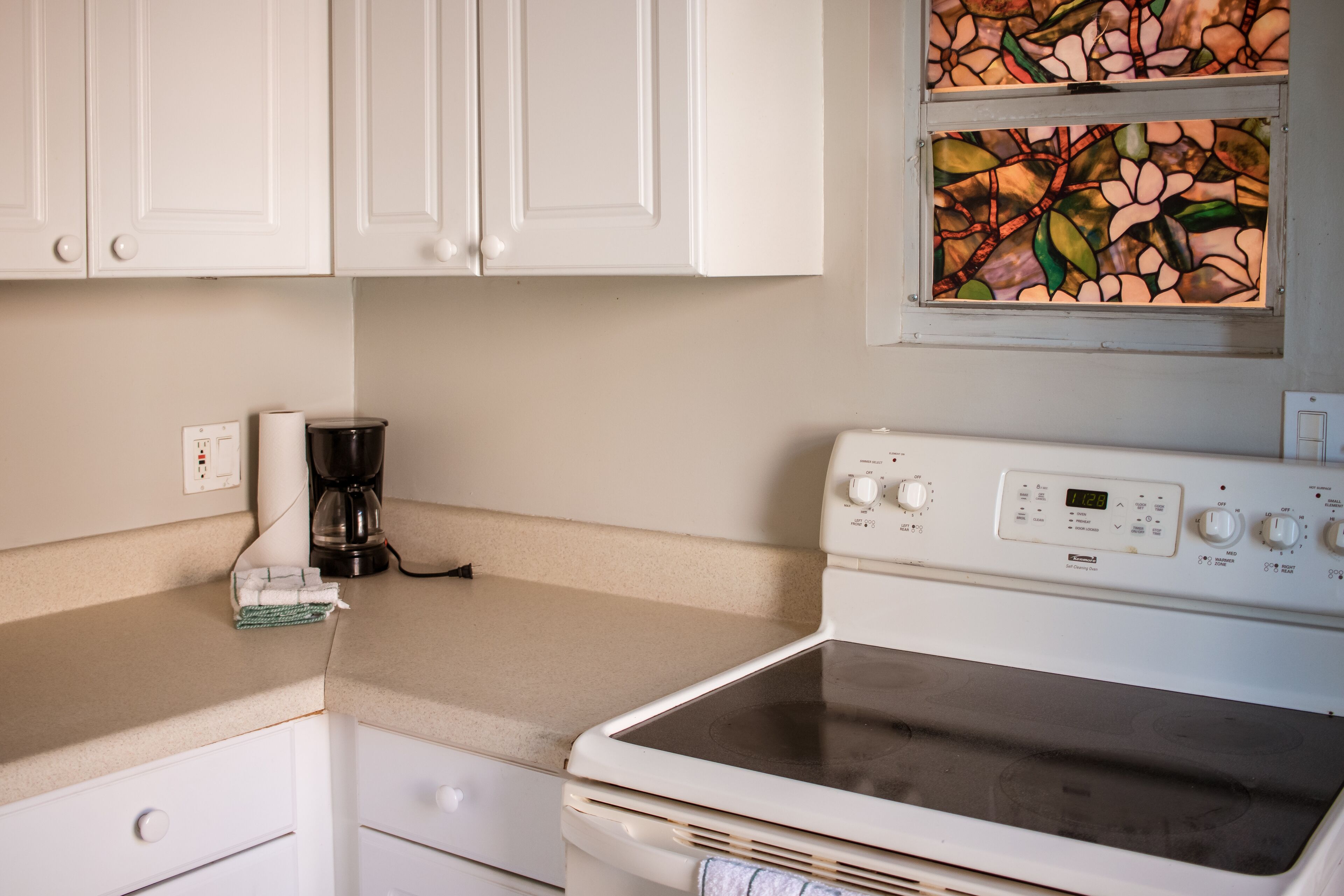 A kitchen with white cabinets, a stove, and a coffee maker.