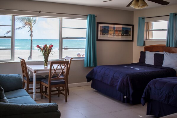 Een hotelkamer met een bed, een bureau met stoel, uitzicht op het strand en een plafondventilator.