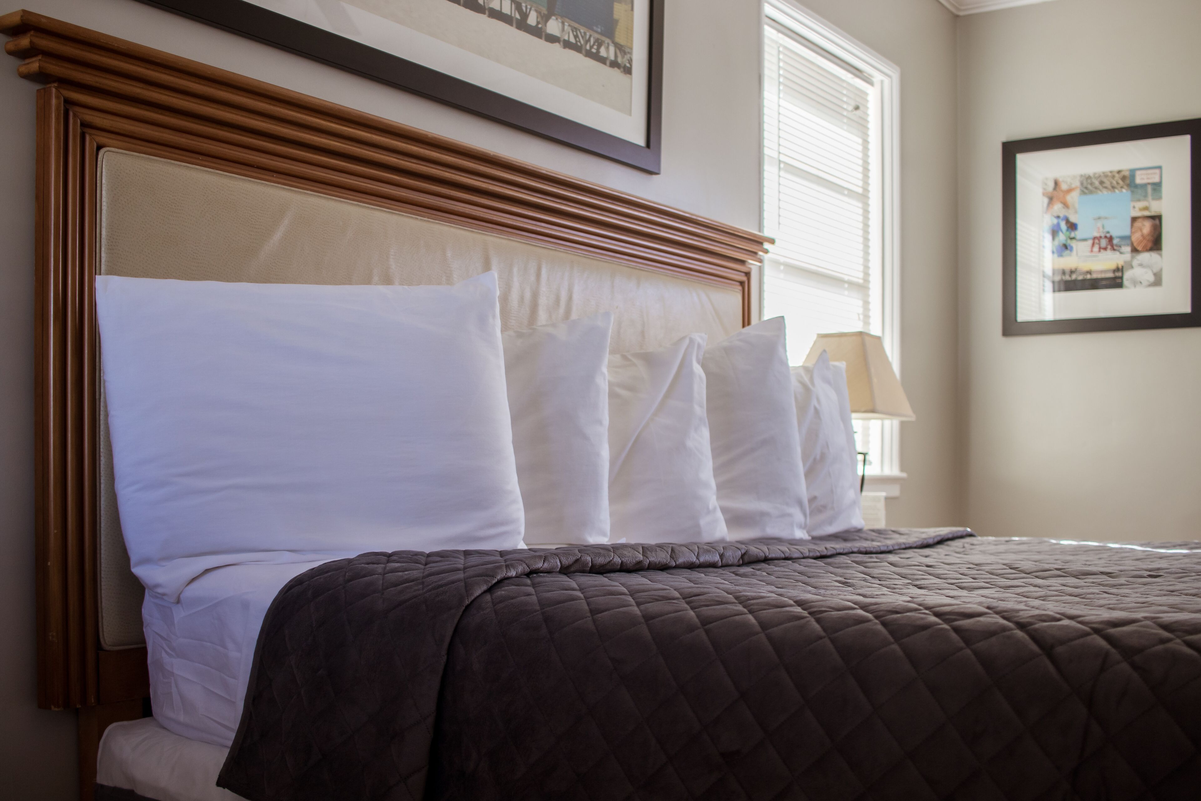A neatly made bed with a brown quilted bedspread and white pillows, a wooden headboard, and a framed picture on the wall.