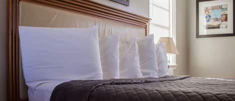 A neatly made bed with a brown quilted bedspread and white pillows, a wooden headboard, and a framed picture on the wall.