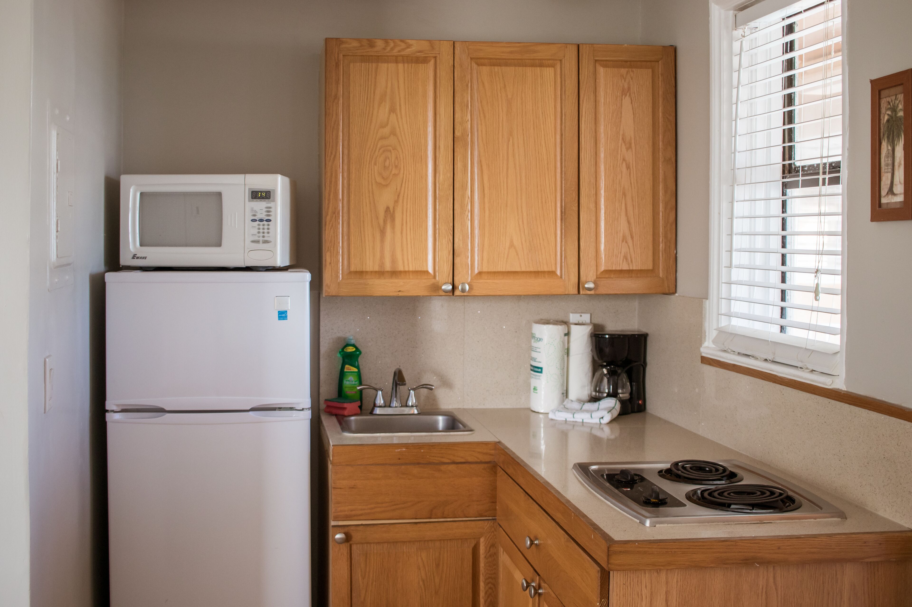 A compact kitchen with wooden cabinets, a white refrigerator, a microwave, a sink, and a stove.