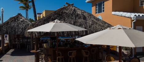 An outdoor seating area with thatched umbrellas, wicker furniture, and a bar.