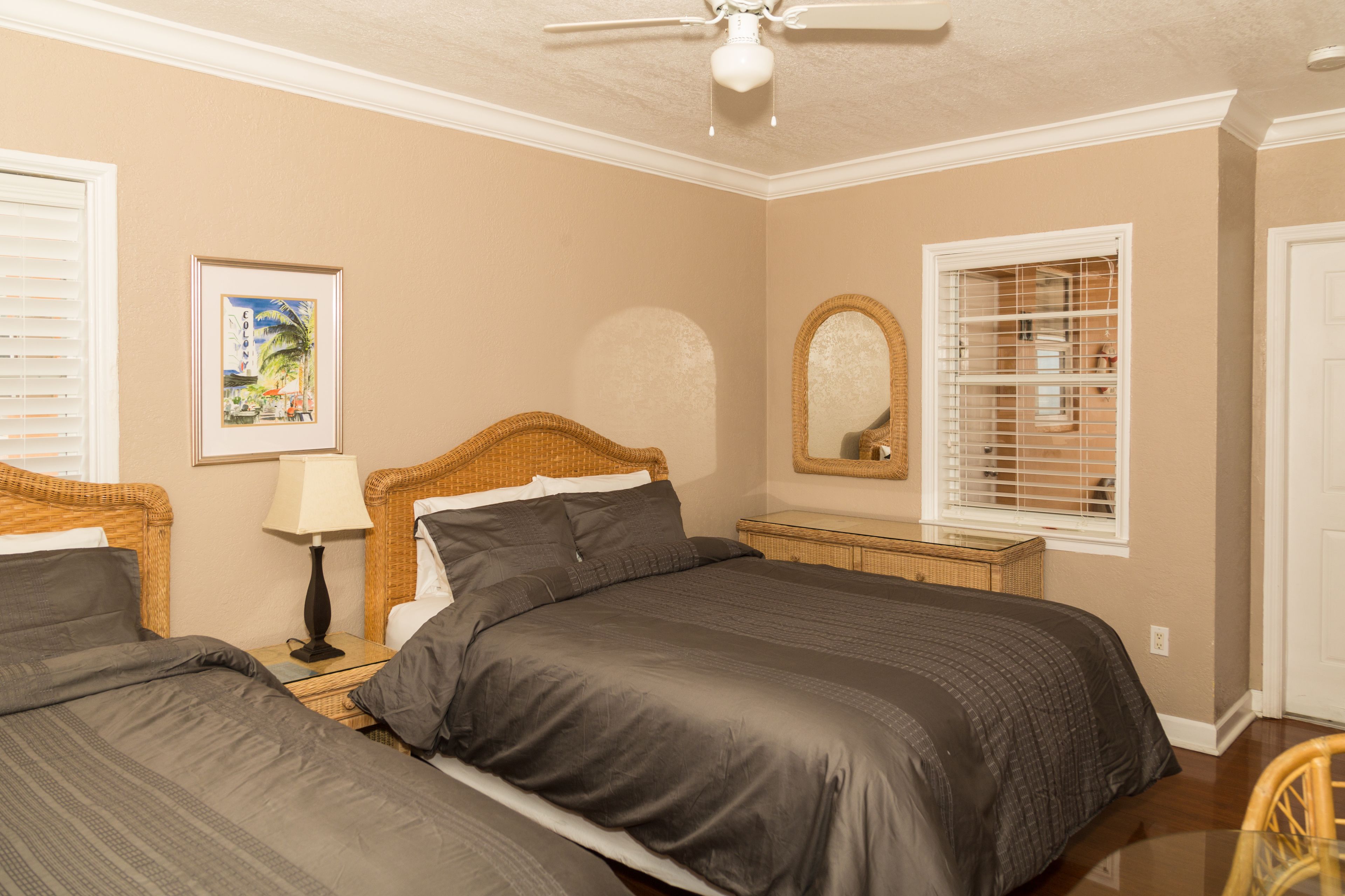 A bedroom with two beds, a ceiling fan, a framed picture, a mirror, and a window with blinds.