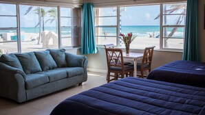 Una habitación con una cama grande, un sofá, una mesa de comedor con sillas y vista a la playa.
