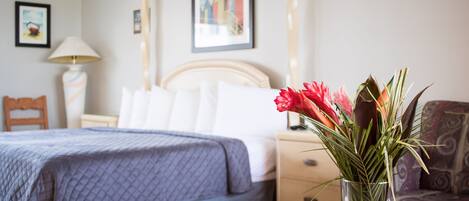 Camera d'albergo con un letto, comodino, lampada e un vaso con fiori.