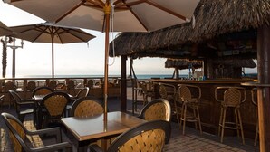 Un área de estar al aire libre con mesas y sillas, un bar y vistas al océano.