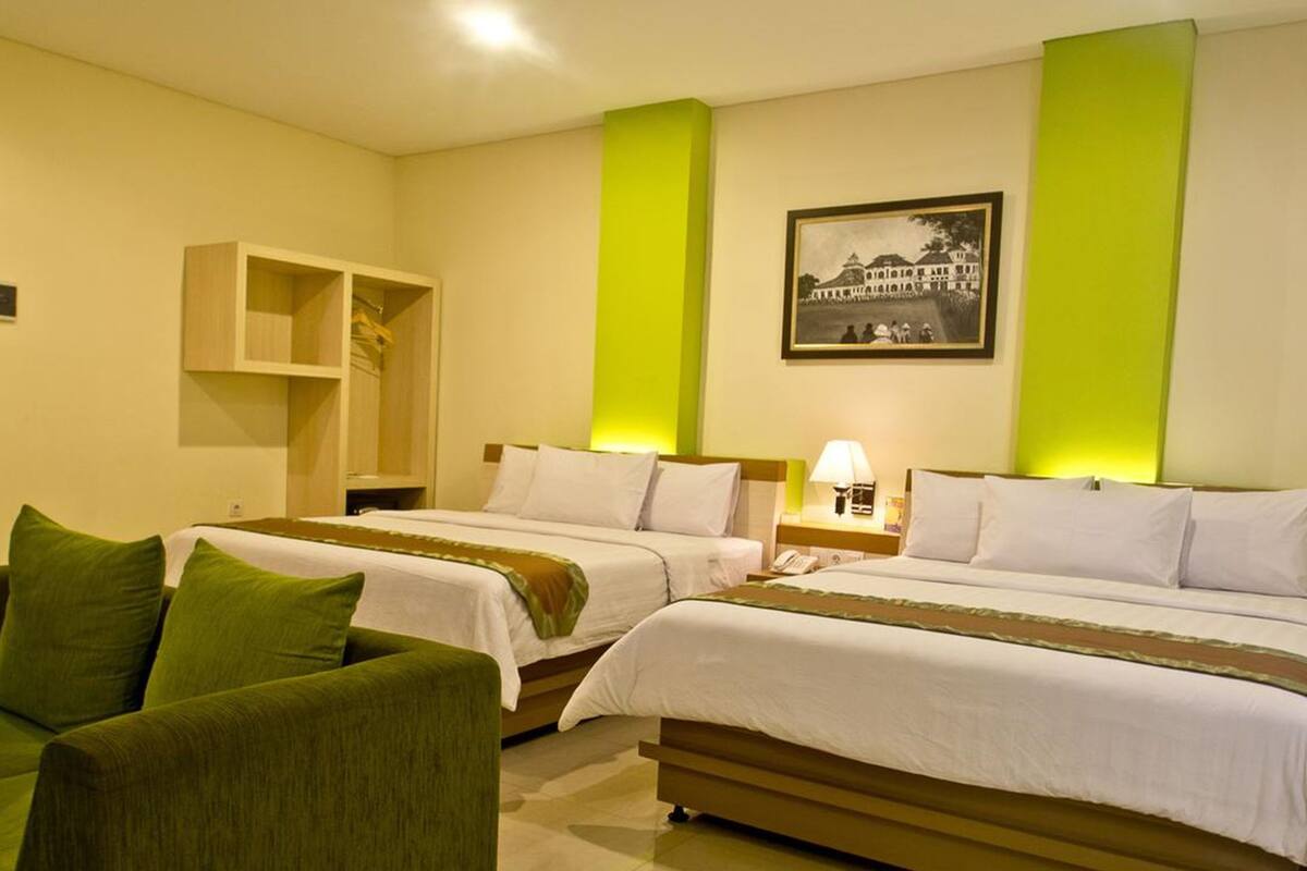A hotel room with two beds, a green sofa, a small wooden cabinet, and a framed picture on the wall.