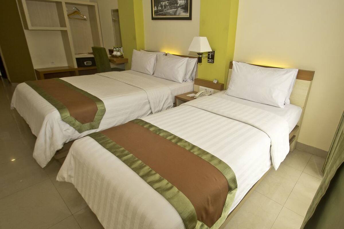 Two single beds with white and brown bedspreads in a hotel room, a nightstand with a lamp, and a small table with a telephone.