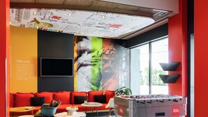 A modern lounge area with a foosball table, comfortable seating, and a large mural. - Ibis Milano Fiera (Lainate)