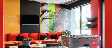 A modern lounge area with a foosball table, comfortable seating, and a large mural.