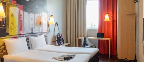 A hotel room with two beds, a desk with a laptop, a guitar, and a wall mural.