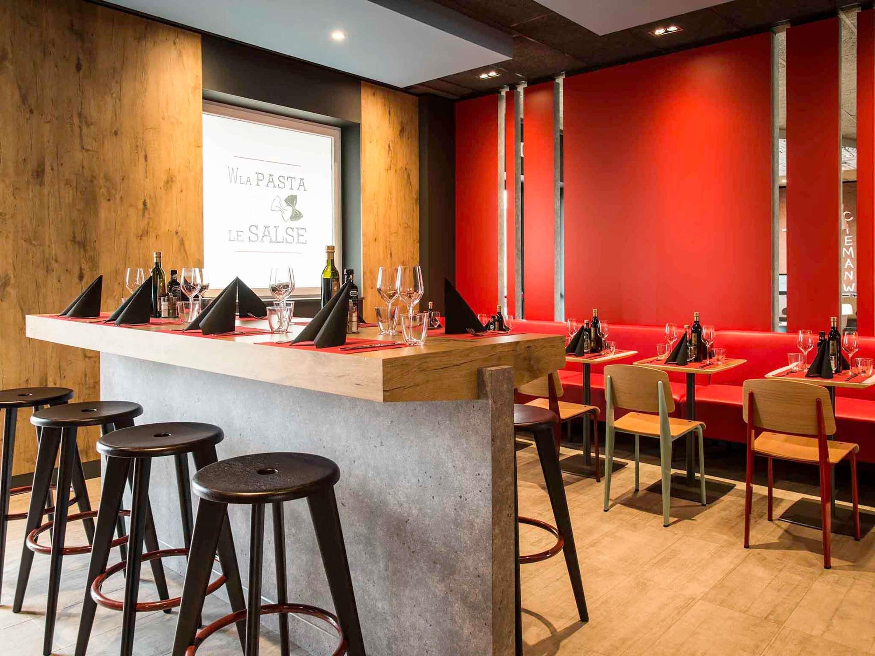Een restaurant interieur met een bar, zitplaatsen en een projectiescherm waarop 'WLA PASTA LE SALSE' staat.