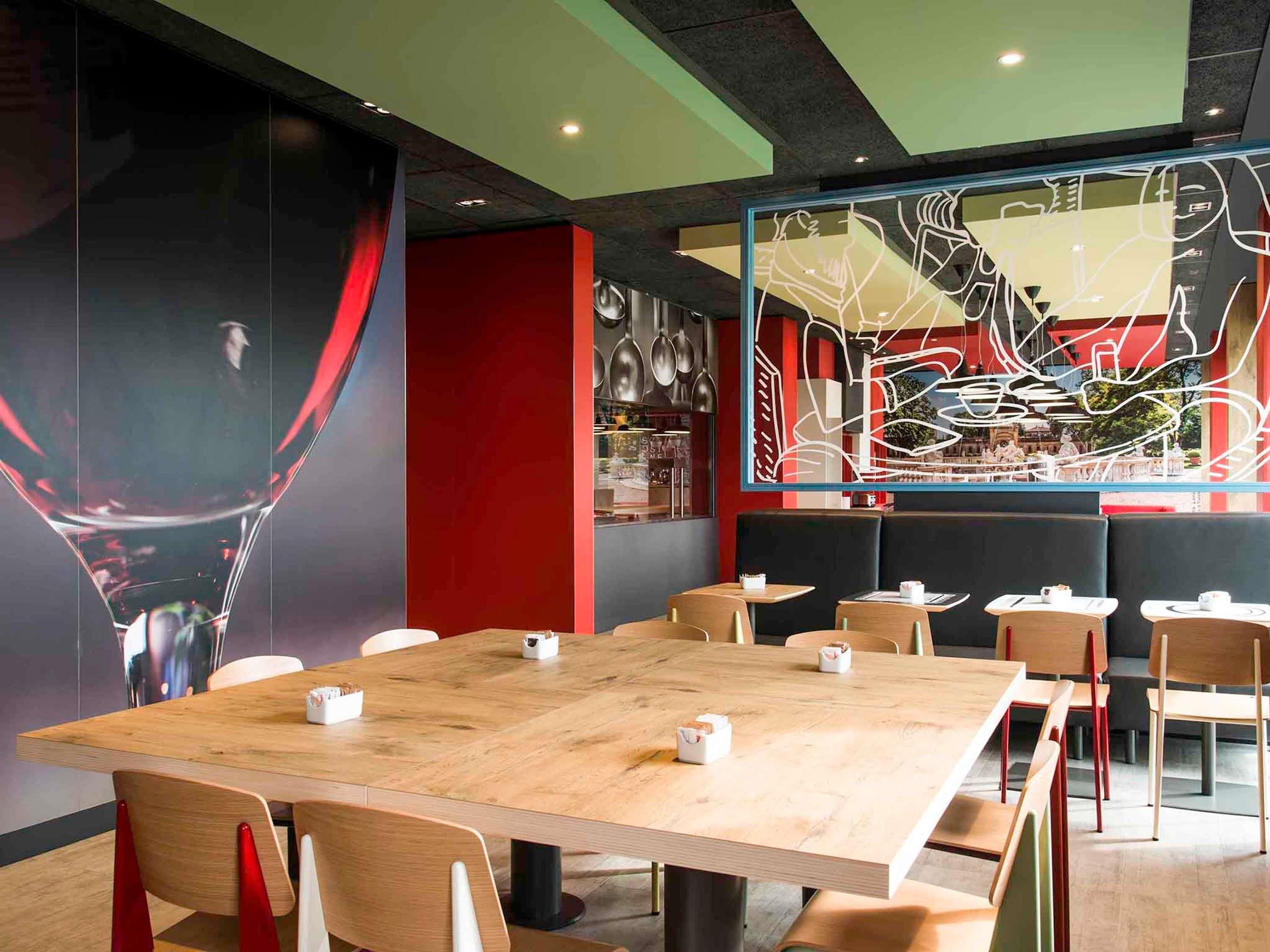 Ein modernes Restaurant-Interieur mit einem großen Holztisch, verschiedenen Sitzgelegenheiten und abstrakter Wandkunst.
