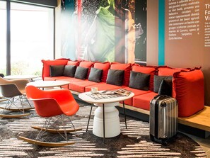 A modern hotel room with a red sofa, a white coffee table, and a red rocking chair. - Ibis Milano Fiera (Lainate)