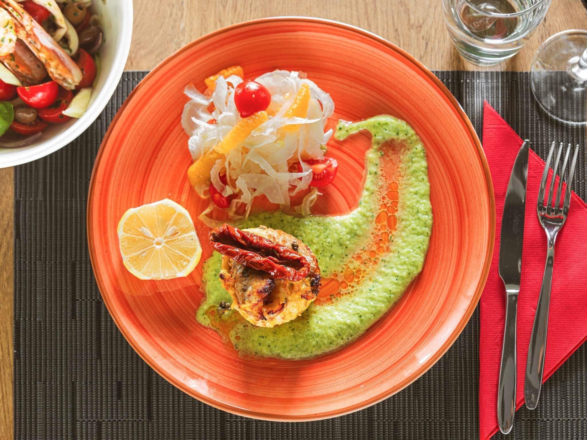 Een bord met een groene saus, een gegrild gerecht en een salade, alles op een oranje bord.