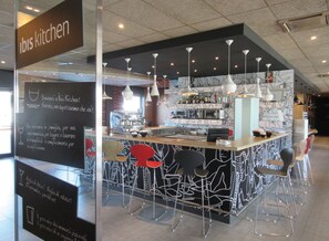 A modern kitchen area with a bar counter, bar stools, and hanging pendant lights. - Ibis Milano Fiera (Lainate)