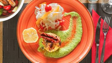 Ein Teller mit grüner Soße, einem gegrillten Gericht und einem Salat mit Kirschtomaten und Zwiebeln.