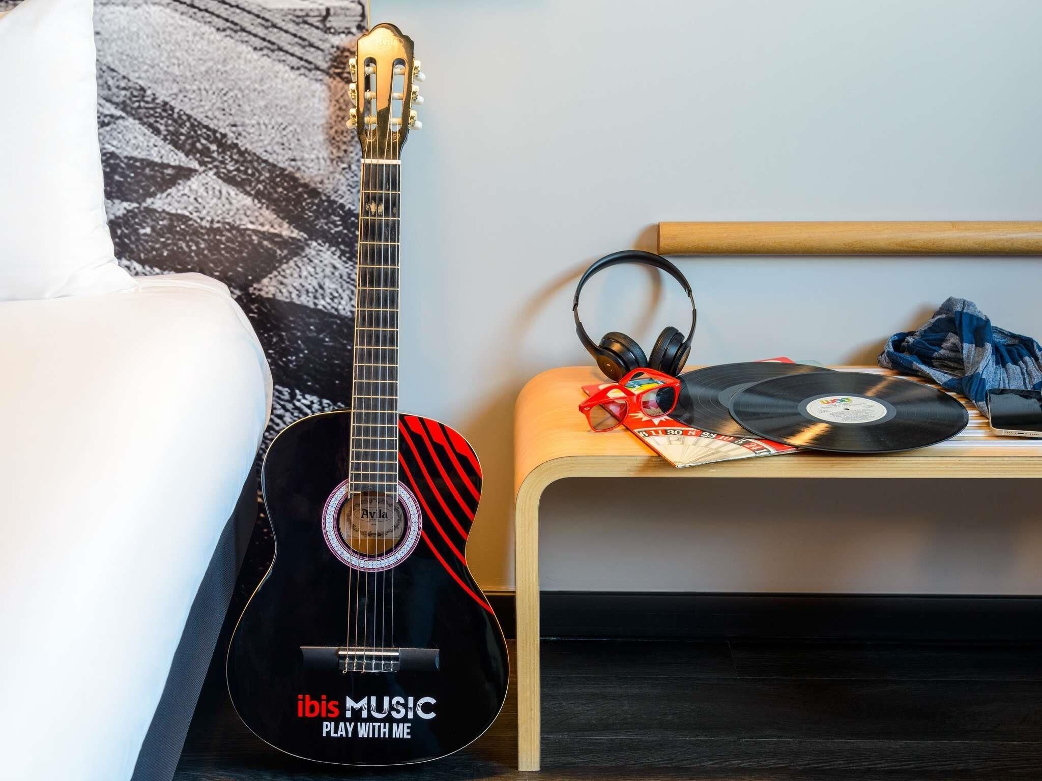A room with a black guitar, headphones, and a record player on a wooden table.