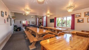 A spacious dining area with wooden tables and benches, large windows with red curtains, and hanging chandeliers. - TripInn Modern Motels & Affordable Accommodation (Westport)