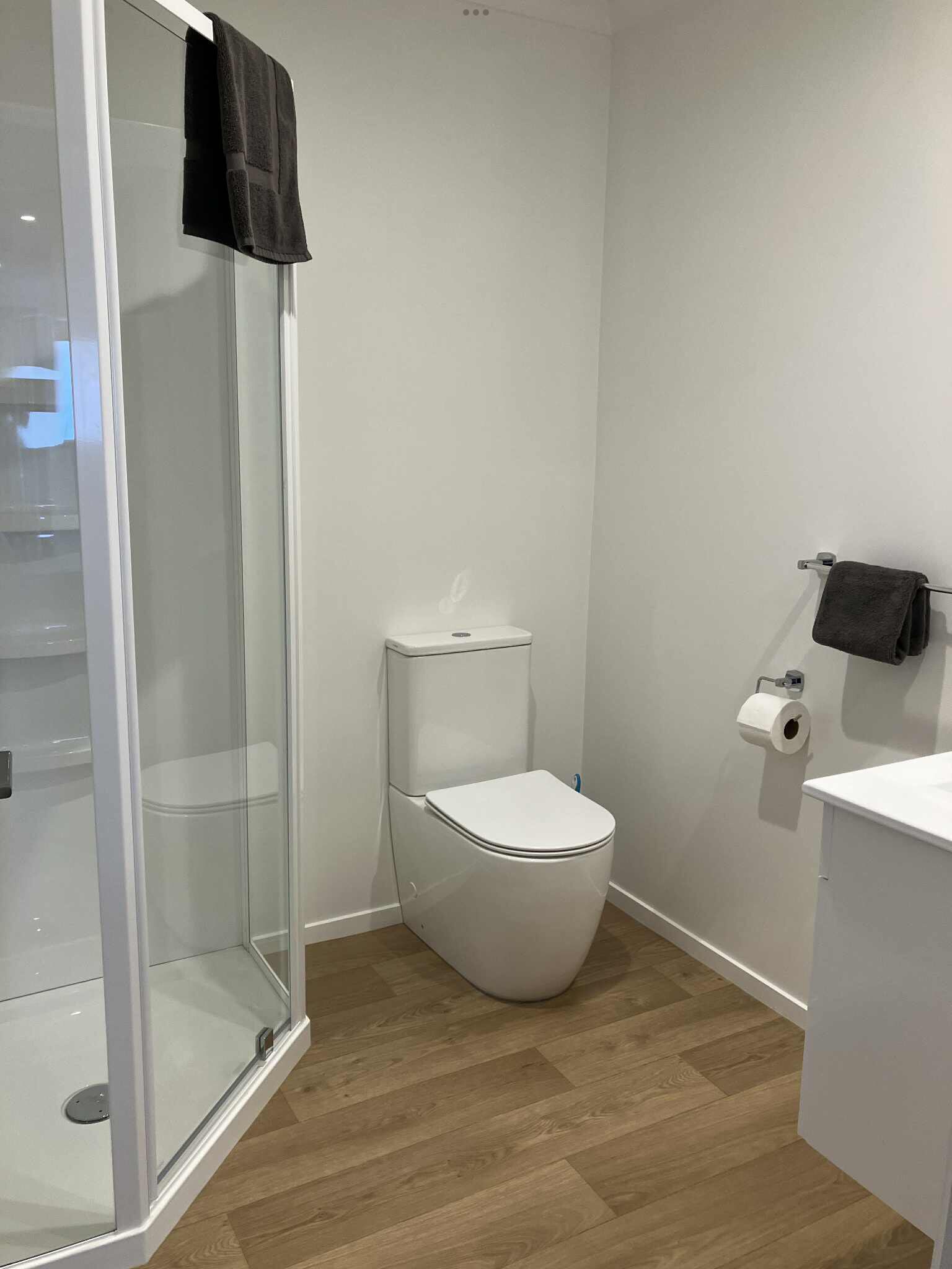 Un baño moderno con cabina de ducha de vidrio, un inodoro blanco y suelo de madera.