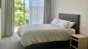 A modern hotel room with a large bed, a bedside table, and a view of greenery outside. - TripInn Modern Motels & Affordable Accommodation (Westport)