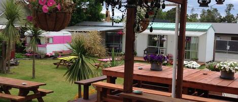 An outdoor patio with wooden tables and benches, hanging flower baskets, and a covered area with lanterns.
