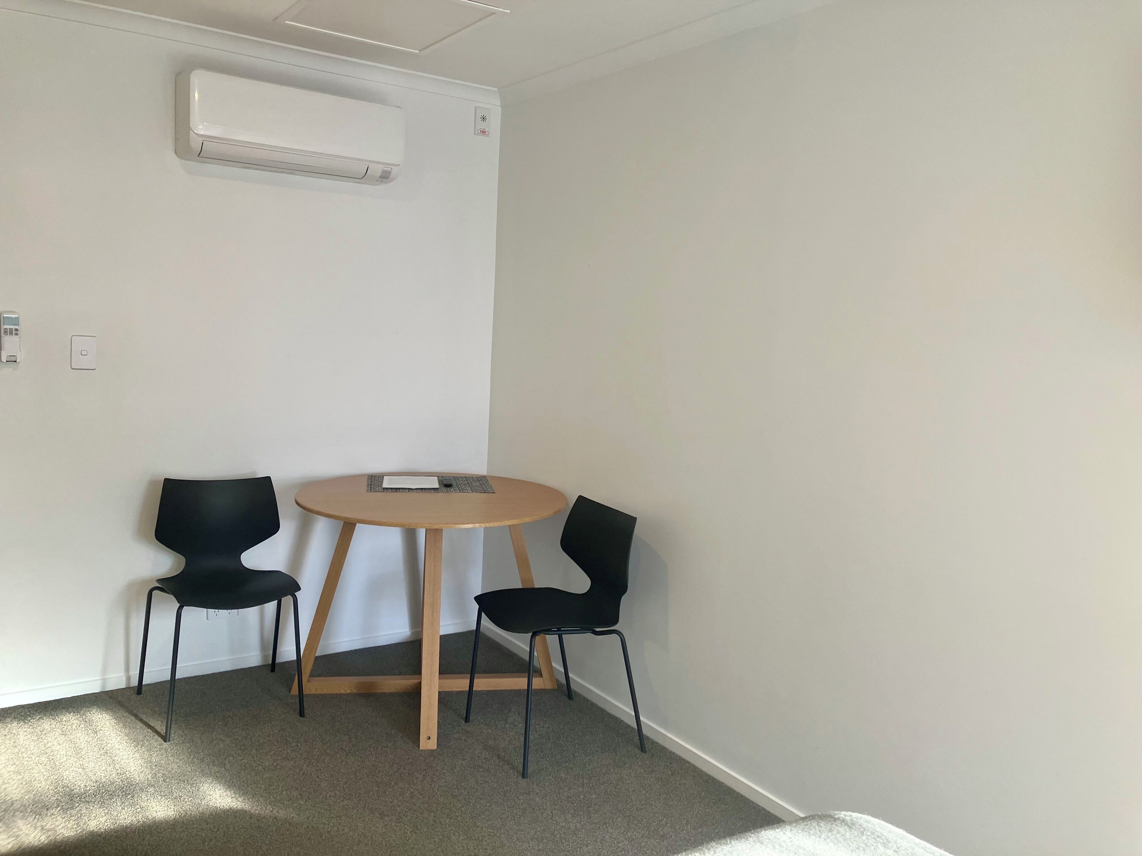 Una habitación con una mesa redonda y dos sillas, un equipo de aire acondicionado y un interruptor de luz en la pared.
