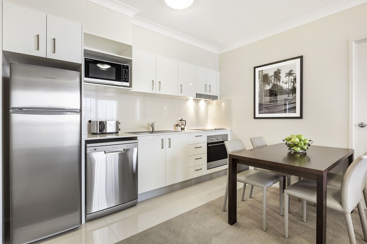 Una cocina moderna con electrodomésticos de acero inoxidable, armarios blancos y un comedor con mesa y sillas.