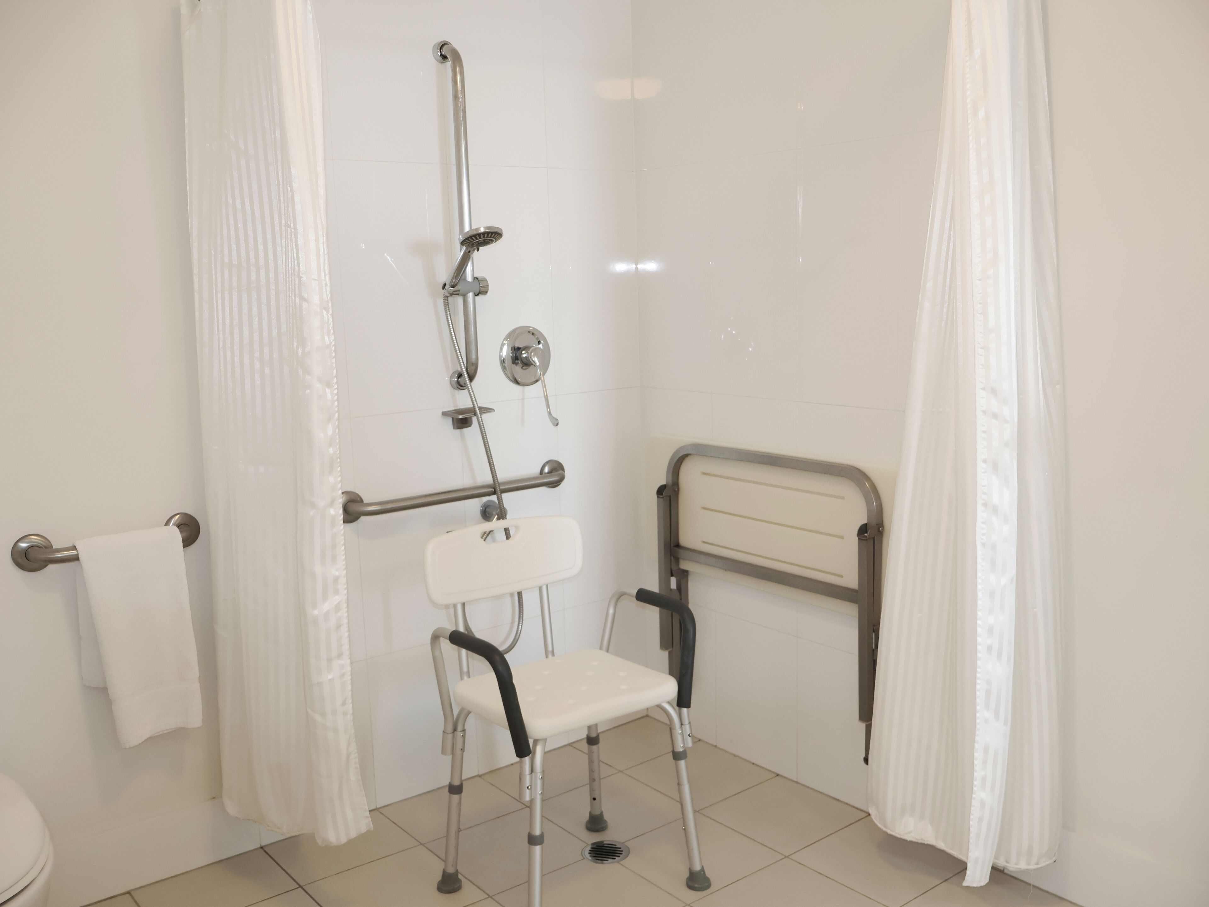 A bathroom with a wheelchair-accessible shower, grab bars, and a toilet with a towel rack.