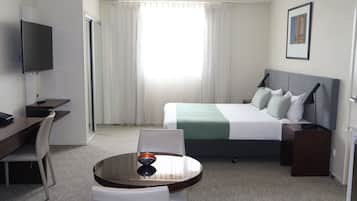 Une chambre d’hôtel avec un lit, un bureau, une chaise, une télévision et une fenêtre avec des rideaux.