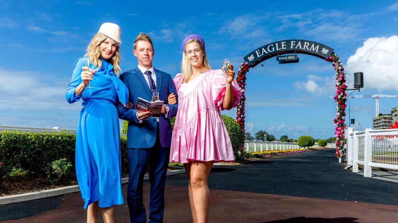Three people standing in front of a sign that reads "EAGLE FARM" with a floral arch.