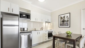 A modern kitchen with stainless steel appliances, white cabinetry, and a dining area with a table and chairs. - Quest Breakfast Creek (Albion)