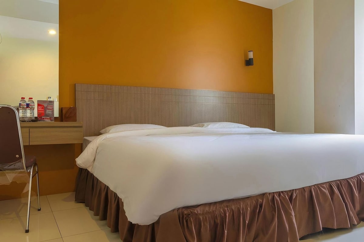A hotel room with a bed, a chair, a nightstand, and a wall-mounted light.