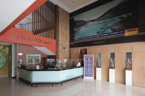 A hotel reception area with a modern design, including a reception desk, a large screen displaying a scenic view, and a signboard for special care services. - Cassadua Hotel (Bandung)