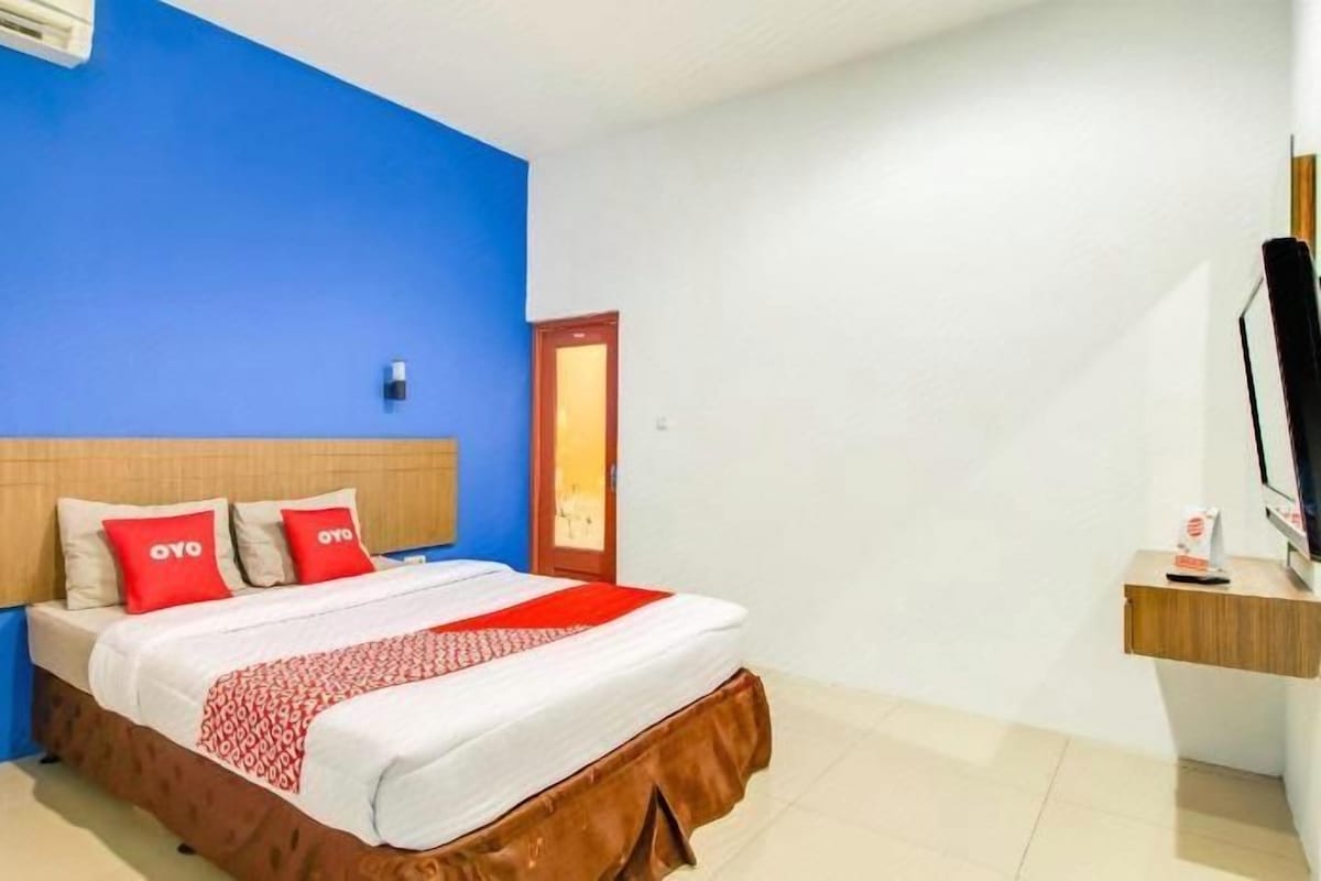 A hotel room with a bed, a bedside table, a TV, and a window.