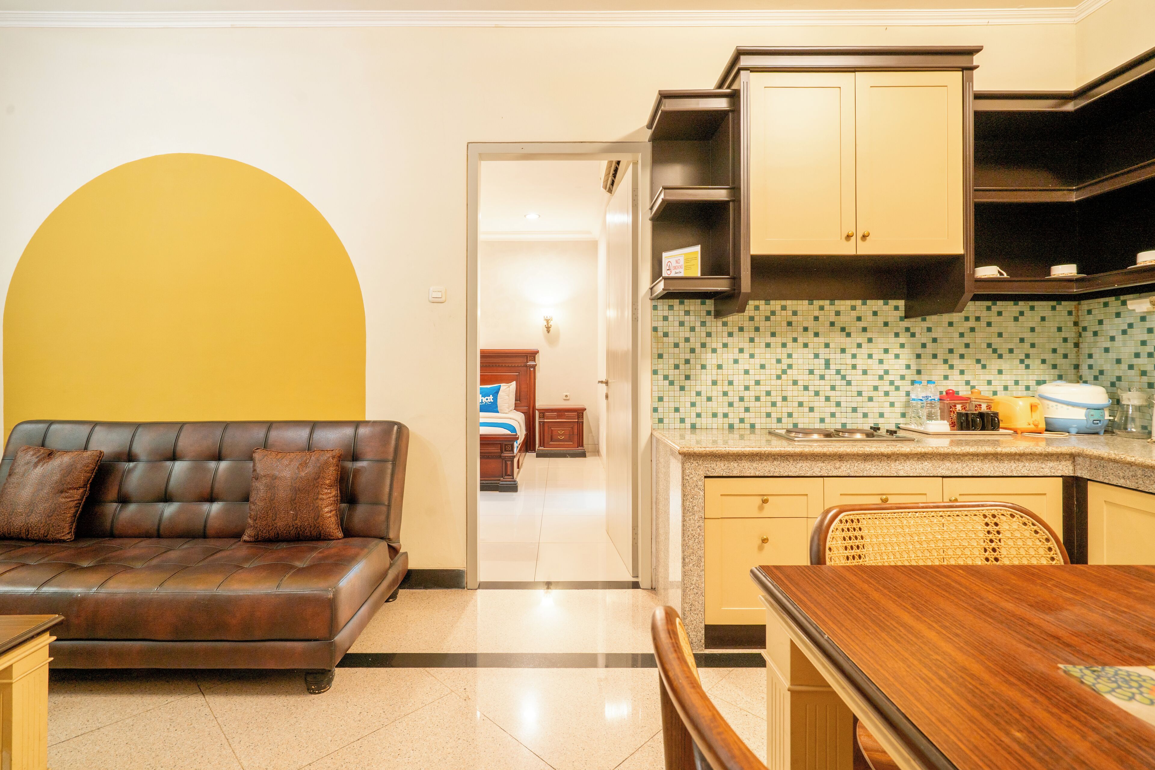 A compact living space with a sofa, a dining table, and a kitchen area with tiled backsplash and wooden cabinets.