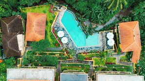Eine Vogelperspektive zeigt einen luxuriösen Urlaubsort mit einem zentralen Schwimmteich, mehreren überdachten Bereichen und üppiger Bepflanzung.