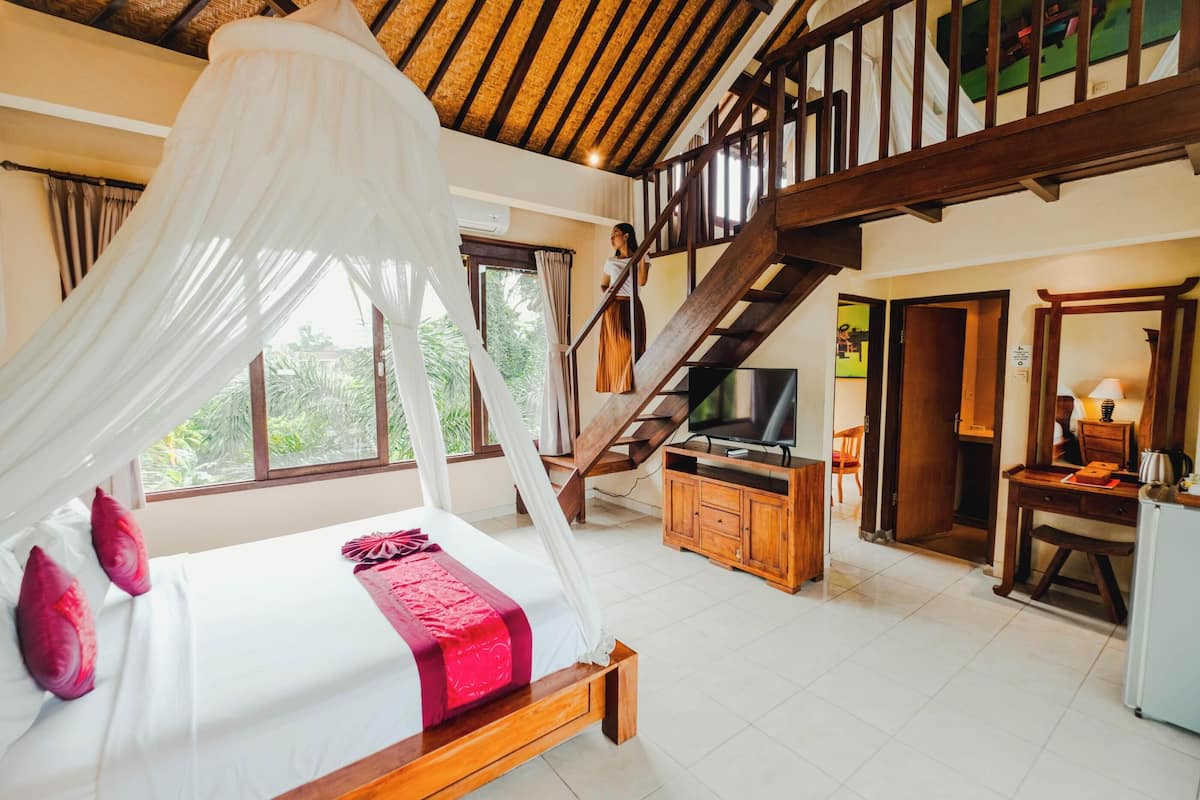 A bedroom with a bed, a TV, a desk, and a staircase.