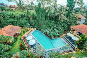 A large swimming pool surrounded by lush greenery and palm trees, with a tiled deck and lounge chairs. - Sri Aksata Ubud Resort (Ubud)