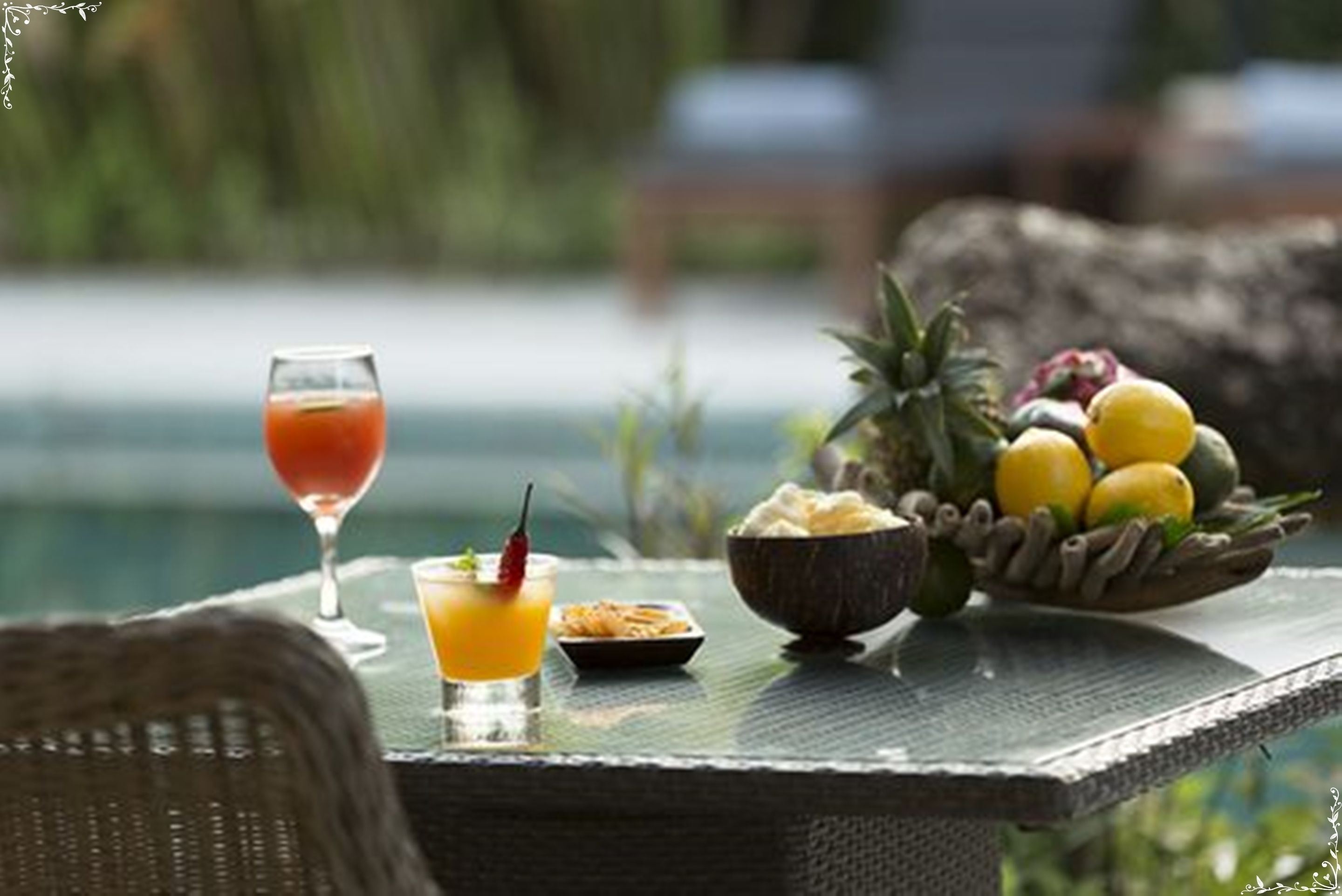 A table with a glass of orange juice, a small dish, and a bowl of fruit including pineapple and lemons.