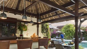 Un área de comedor al aire libre con piscina, asientos cubiertos y un bar.